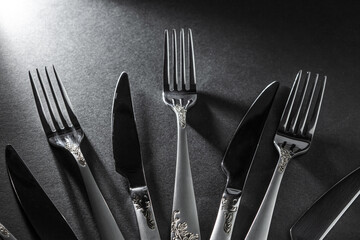Forks and knives on a black background. The shadow of the cutlery falls to the surface. Black and white photography.