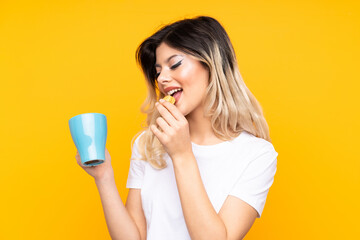 Teenager girl isolated on yellow background holding colorful French macarons and a cup of milk