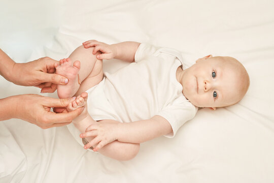 Cute small boy lying at bed. Childhood concept. Light background. Serious child. Copyspace. Stay home. Onesie mockup. Foot massage. White clothes
