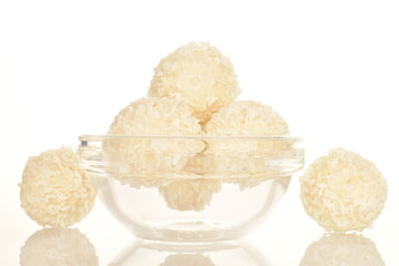 Several round sweets with coconut flakes in a glass bowl, close-up, isolated on white.