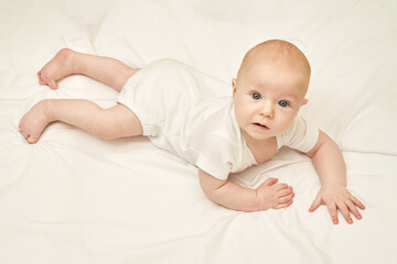 Cute small boy lying at bed. Childhood concept. Light background. Serious child. Copyspace. Stay home. Onesie mockup. White clothes