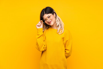 Teenager girl isolated on yellow background with glasses and happy