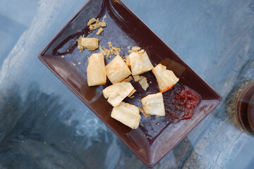 fried cassava with hot sauce on a plate on a glass table
