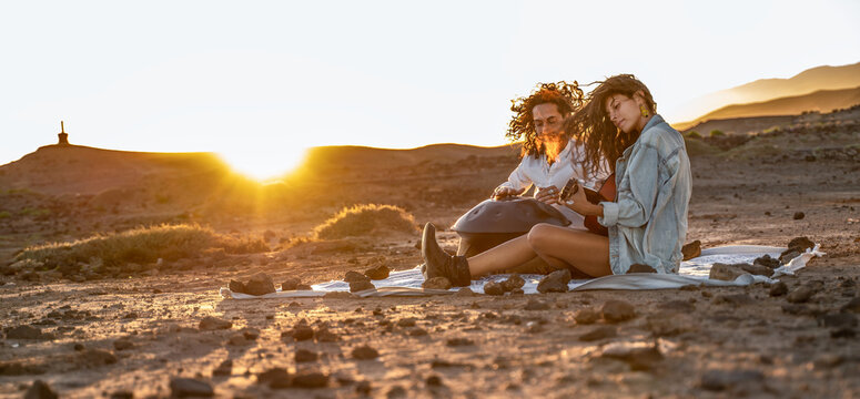 Hippie loving couple playing on guitar and hangdrum in the nature. Picnic during beautiful sunset on Tenerife. Real people lifestyle and hobby concept.