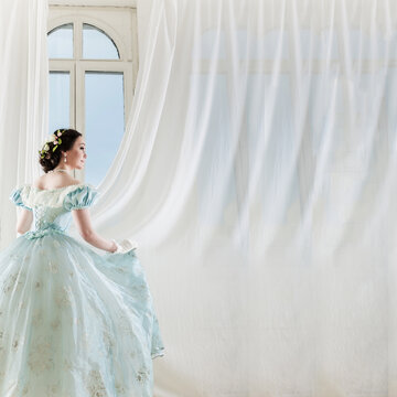 A beautiful elegant dark haired woman in a historic 1867 dress on background with window. High quality photo