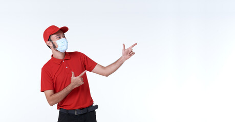 Fototapeta na wymiar Asian delivery man wearing face mask in red uniform with his finger pointing to copy space isolated over white background. social distancing and new normal concept.