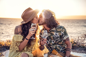 Fashionable boho couple with wine having romantic date on sunset beach, kissing, spending time together. Real people emotions and love concept. © neonshot