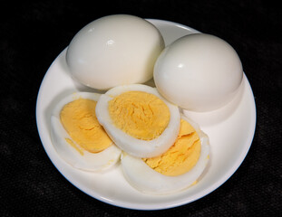 Boiled chicken egg on a white plate. A cut egg with a yellow yolk. Boiled egg cutaway. Breakfast. Close-up. Black background