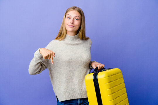 Young russian woman holding suitcase to travel points down with fingers, positive feeling.