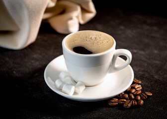 White cup of coffee on a saucer with coffee beans and marshmallows. Espresso. Close-up.