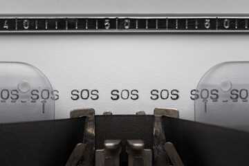 Typing text SOS on vintage manual typewriter. Close up of writes word on white paper. Typing a...