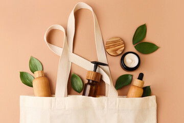 Open eco friendly cotton reusable bag with the different containers from the wood and glass.Pastel colors.Fresh natural leafs around.Concept of organic,zero waste cosmetics.Woman bag with accessories.