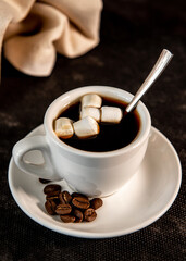 White cup of coffee on a saucer with coffee beans and marshmallows. Espresso. Close-up.