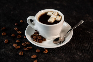 White cup of coffee on a saucer with coffee beans and marshmallows. Espresso. Close-up.
