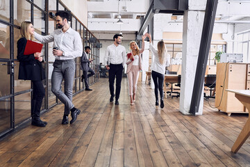 On the way to business meeting. Full length of young modern people in formal wear having a discussion while walking through the office. A couple of freelancers are give five to each other