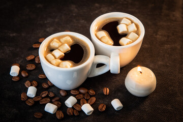Two cups of coffee with small marshmallows and candles on the table. Coffee, coffee beans, marshmallows. Dark background. Close-up
