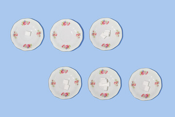 Creative pattern made with saucers and sugar cubes on pastel blue background. Retro aesthetic style flat lay. Spring idea. Trendy concept.