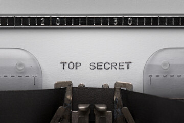 Typing text TOP SECRET on vintage manual typewriter. Close up of writes word on white paper. Shot in macro.
