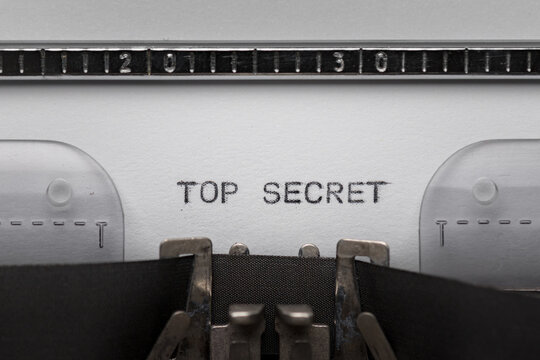 Typing text TOP SECRET on vintage manual typewriter. Close up of writes word on white paper. Shot in macro.