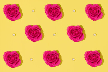 Creative pattern made with  magenta colored rose and white pearls on bright yellow background. Minimal aesthetic flat lay. Romantic creative idea. Spring or summer concept with bloom.
