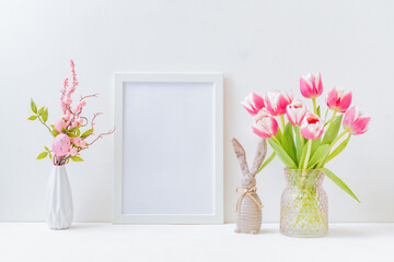 Home interior with easter decor. Mockup with a white frame and willow branches, pink tulips in a vase on a light background