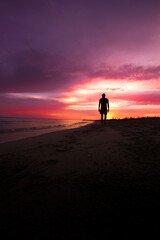 Persona a contraluz, caminando por la playa mientras el el amanecer de un hermoso cielo lo deja a oscuras.