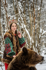 beautiful russian girl in national costume with a brown bear in the winter forest