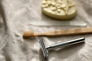 Fototapeta premium Sustainable toiletries on linen cloth: reusable metal safety razor, wooden toothbrush, glass nail file and soap bar. Selective focus.
