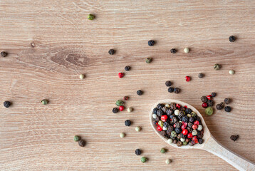 Wooden spoon with different kinds sort of peppercorns on wooden background. Top view. Copy space.