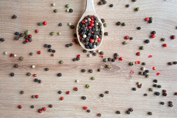 Wooden spoon with different kinds sort of peppercorns on wooden background. Top view. Copy space.