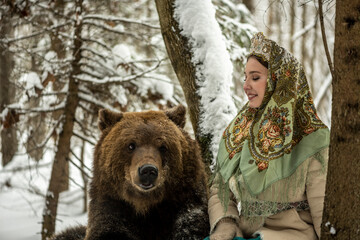  beautiful russian girl in national costume with a brown bear in the winter forest