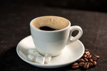 White cup of coffee on a saucer with coffee beans and marshmallows. Espresso. Close-up.