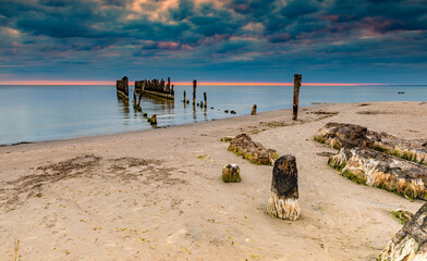 Old broken fishing pier at sandy beach of the Baltic Sea at sunset, concept of ecological tourism