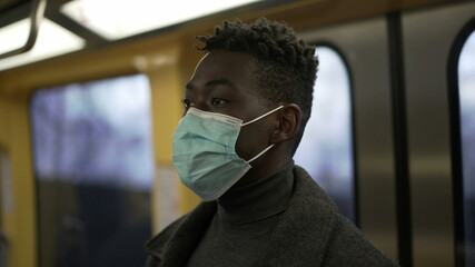 African man standing in subway metro wearing coronavirus mask underground commute