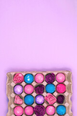 Easter eggs painted with gouache and dried flowers in egg box on violet pink background, copy space, vertical image