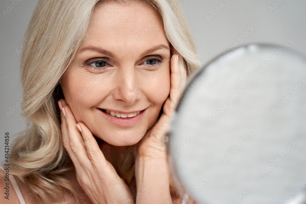 Poster happy 50s middle aged woman model touching face skin looking in mirror. smiling mature older lady pa