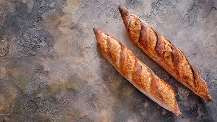 Two freshly baked baguettes on a stone background.