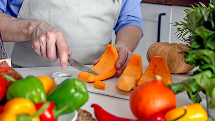 Male hands are cutting an orange pumpkin with a knife on the board at the kitchen table. Home cooking vegan healthy food concept