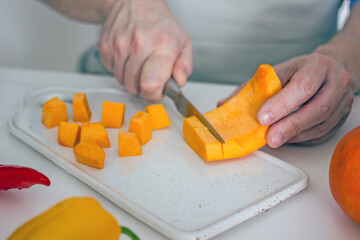Male hands are cutting an orange pumpkin with a knife on the board at the kitchen table. Home cooking vegan healthy food concept