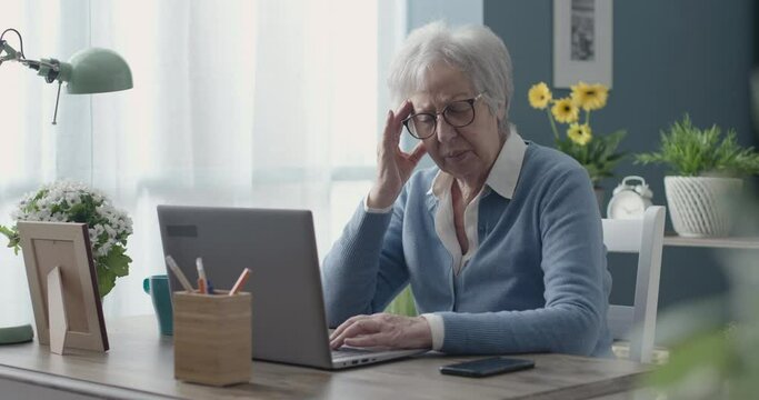 Tired elderly woman using her laptop and having a headache