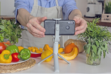 A man without a face, a food blogger, uses his phone to photograph the process of preparing food in his kitchen from vegetables.Concept of making vegan food from natural products at home, self-care, 