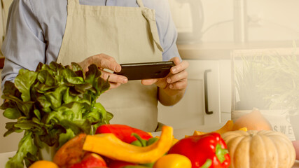 A man without a face, a food blogger, uses his phone to photograph the process of preparing food in his kitchen from vegetables.Concept of making vegan food from natural products at home, self-care, 