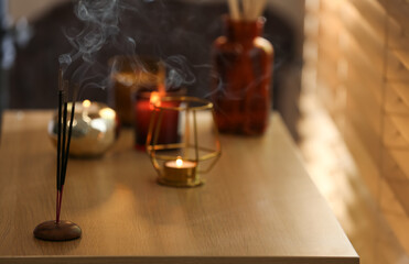 Fototapeta na wymiar Incense sticks smoldering on wooden table near window in room. Space for text