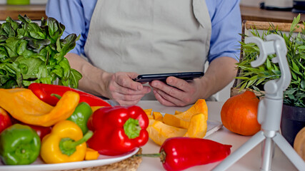 A man without a face, a food blogger, uses his phone to photograph the process of preparing food in his kitchen from vegetables.Concept of making vegan food from natural products at home, self-care, 