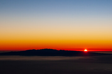 Sunrise red sun behind Canary Island La Gomera in sea. View from Pico del Teide mountain in El Teide National park. Tenerife, Canary Islands, Spain