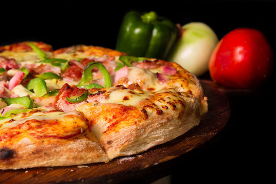 Pizza de queso mozzarella con pepperoni con piment&oacute;n, fondo con tomate, cebolla, piment&oacute;n, fondo negro.