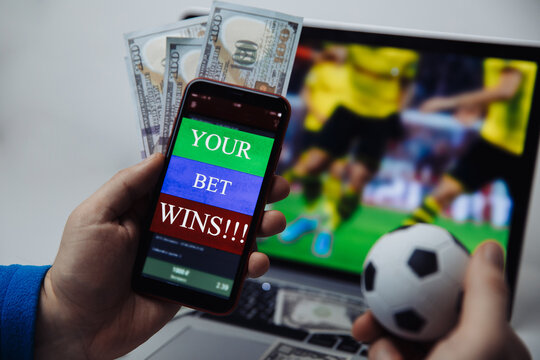 Smartphone with victory message and male's hand with soccer ball. Sport and betting concept.