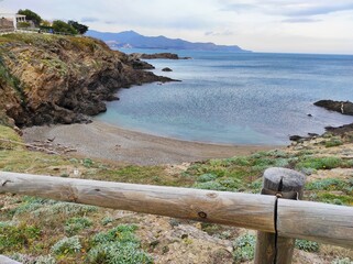Mar en calma, con montañas al fondo, vista desde el camino de ronda junto a una pequeña y vacía...