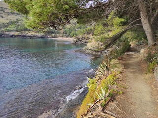 Camino de ronda junto al mar, llegando a la Cala Calitja, una pequeña playa con arena gruesa en un entorno natural de rocas y vegetación 