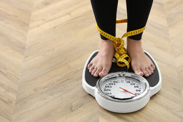 Closeup view of woman tied with measuring tape using scale on floor, space for text. Overweight problem after New Year party